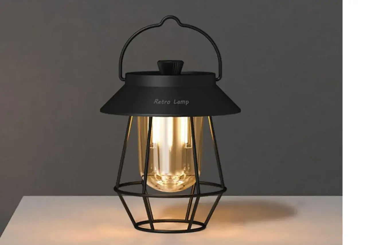 En svart, retro lampa med ett bärhandtag och en glasbehållare som ger ett varmt sken.