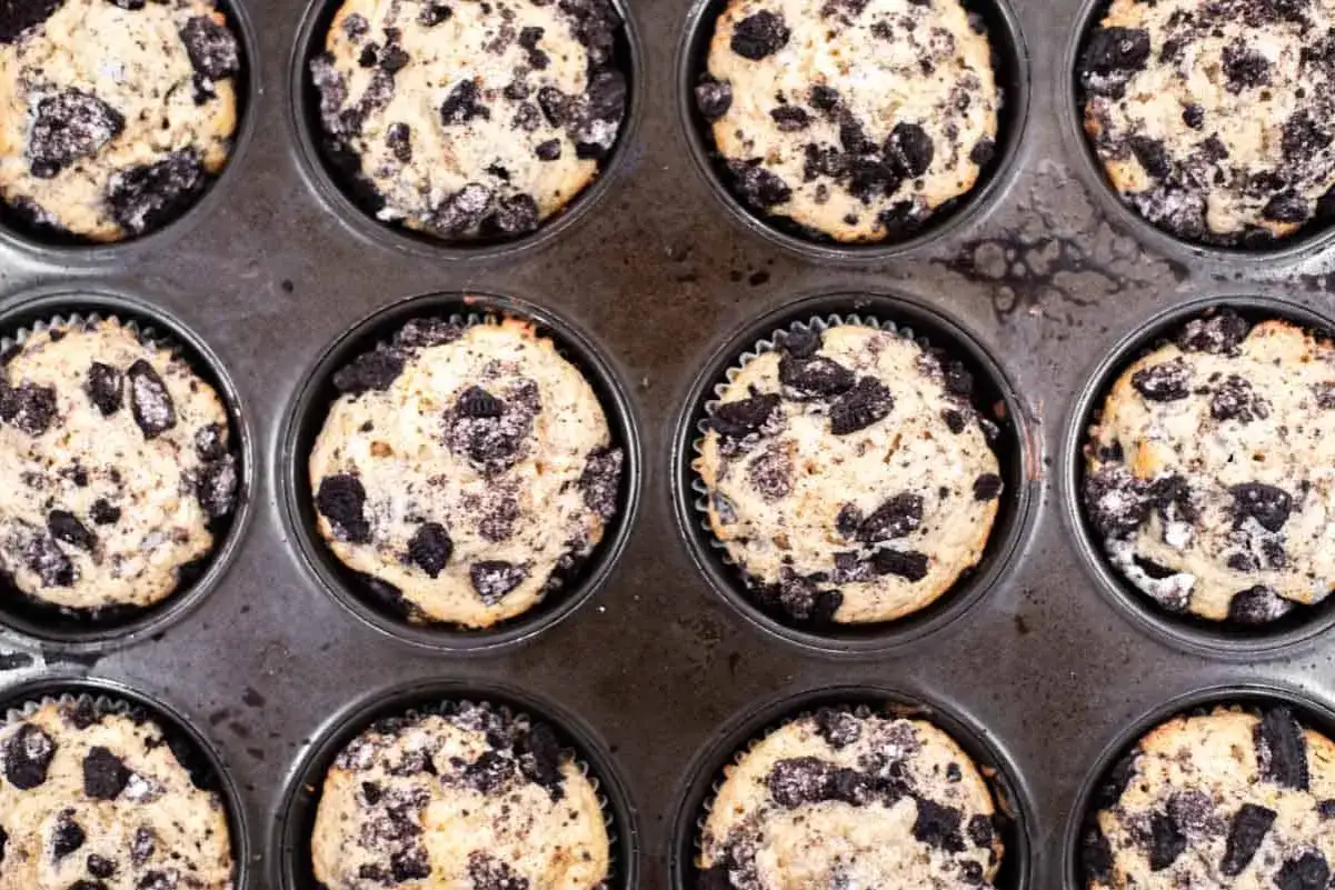 Zwölf frisch gebackene Oreo Muffins in einer Muffinform.