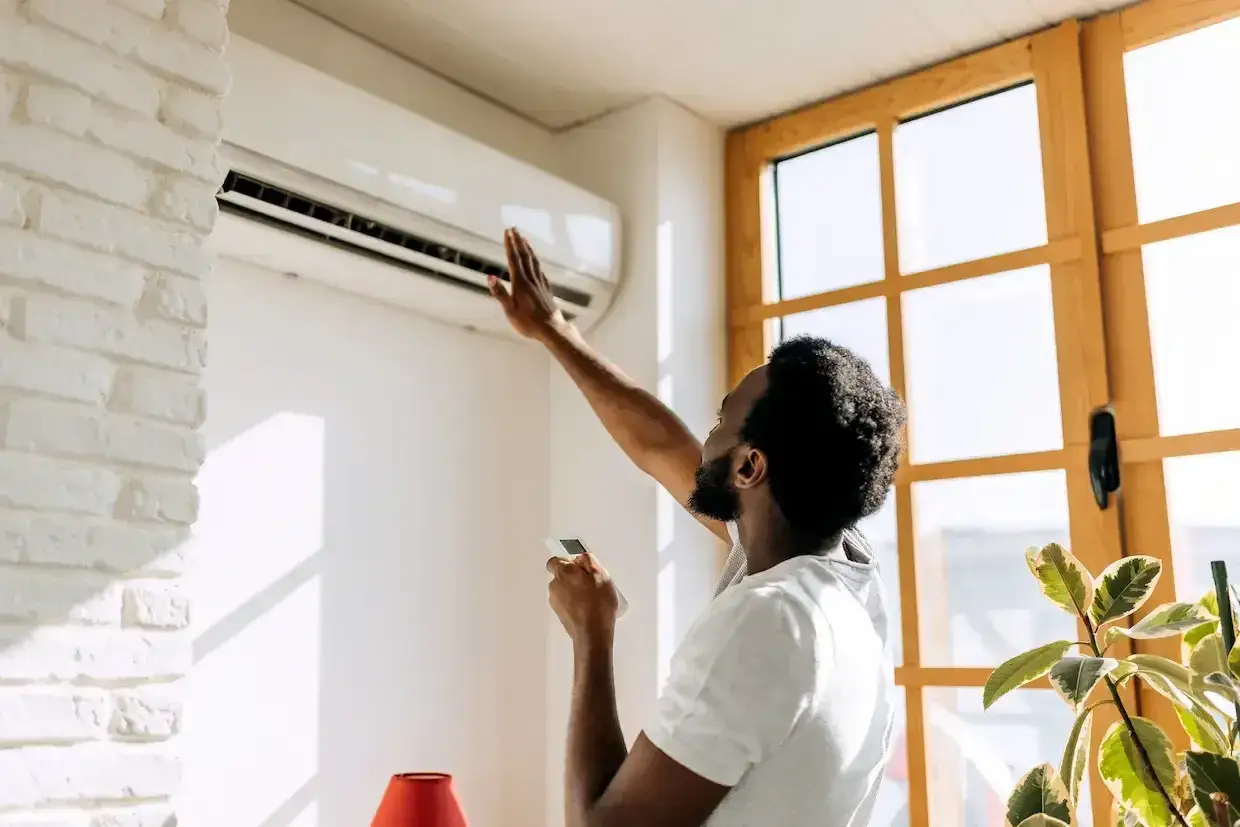 Un homme vérifie sa climatisation murale, prêt à recharger clim maison pour un confort optimal.