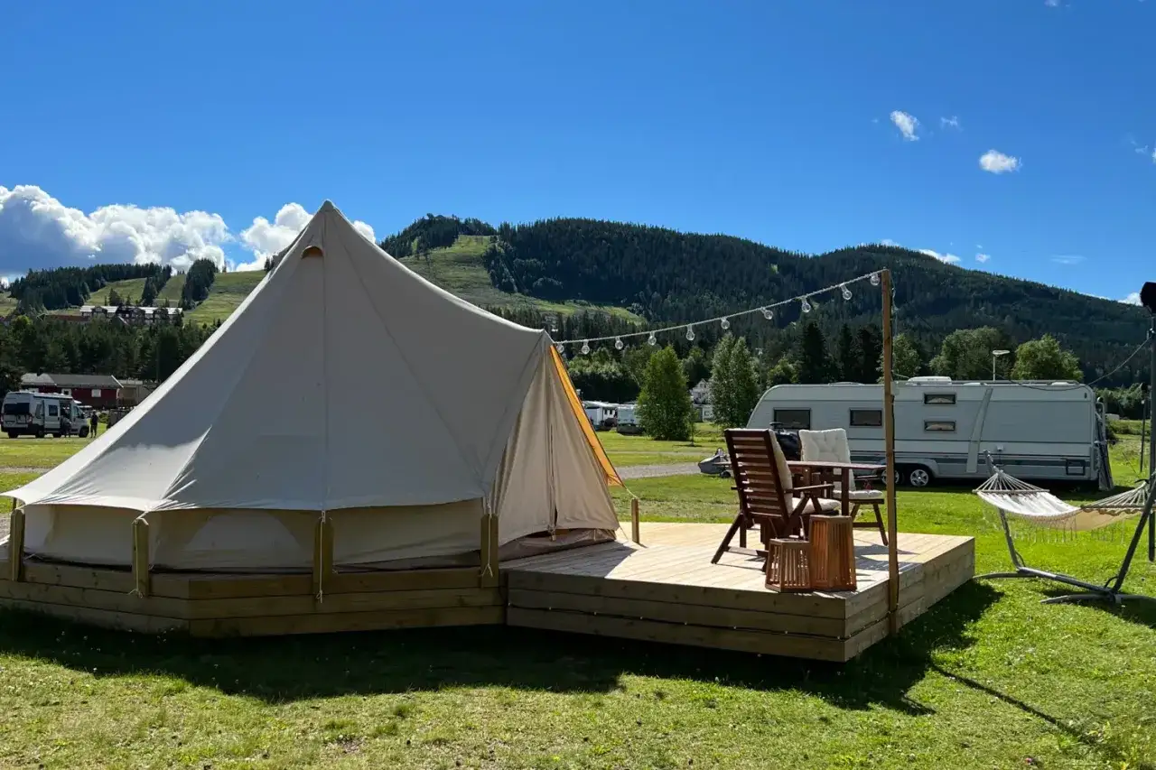 En glampingtält med altan, möbler och hängmatta. En husvagn syns i bakgrunden. Perfekt för din packlista camping.