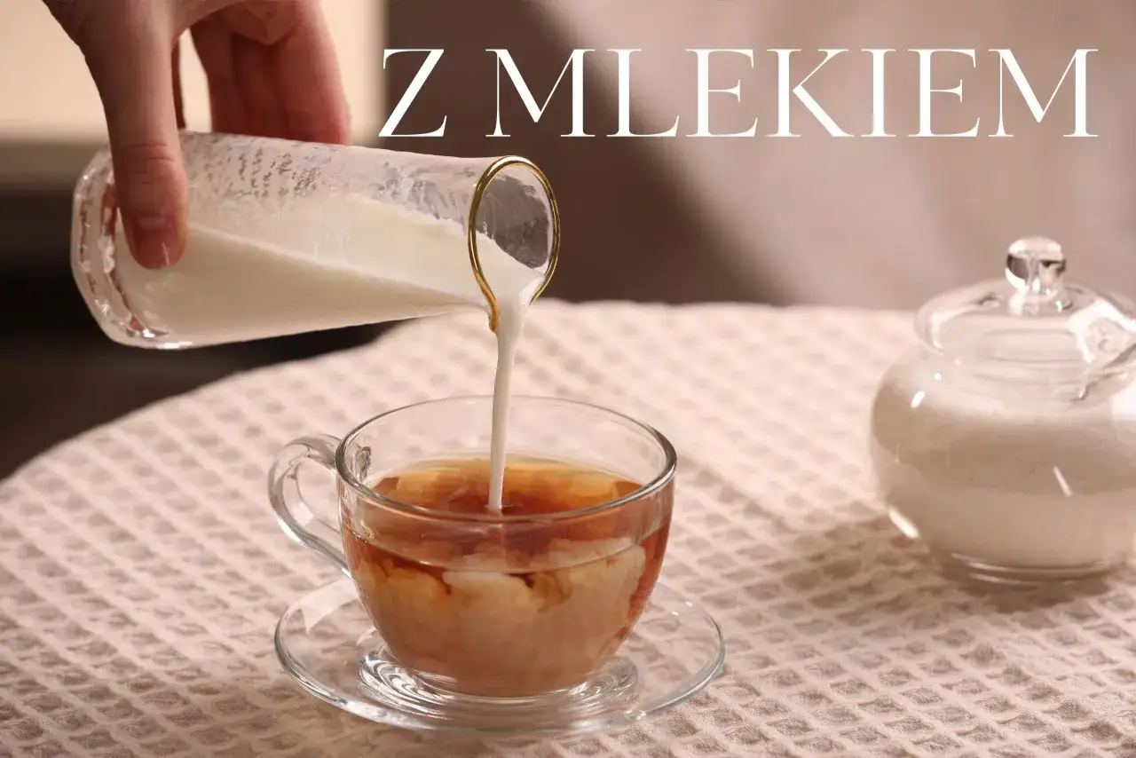 Ręka wylewa mleko do szklanki z herbatą, tworząc piękne smugi. Obok stoi cukiernica. Idealna herbata z mlekiem na chłodny dzień.