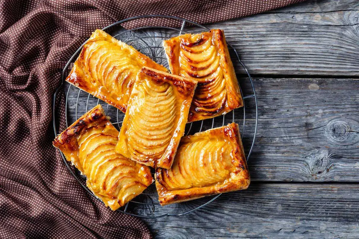 Deliziosi dolci con pasta sfoglia e mele caramellate, disposti su una griglia di raffreddamento su un tavolo di legno rustico.