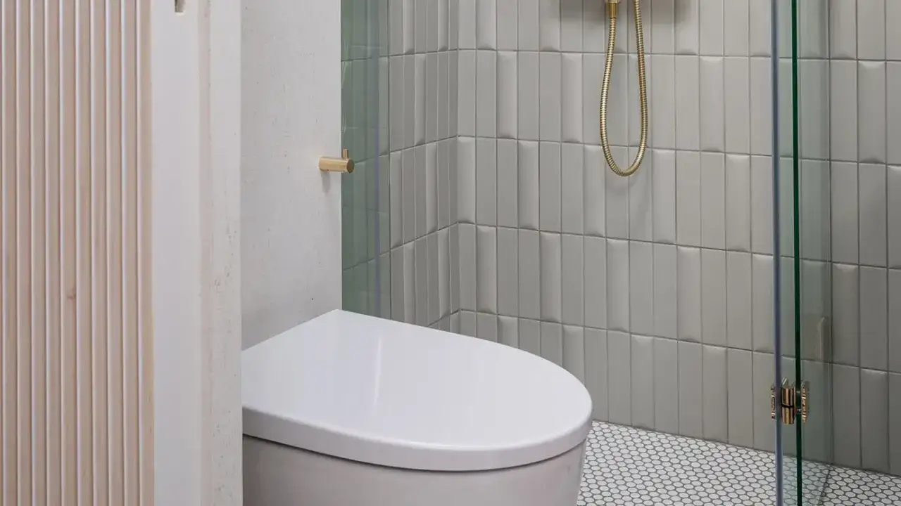 Modernas reformas de baños ideas: inodoro blanco, ducha con azulejos grises y detalles dorados.