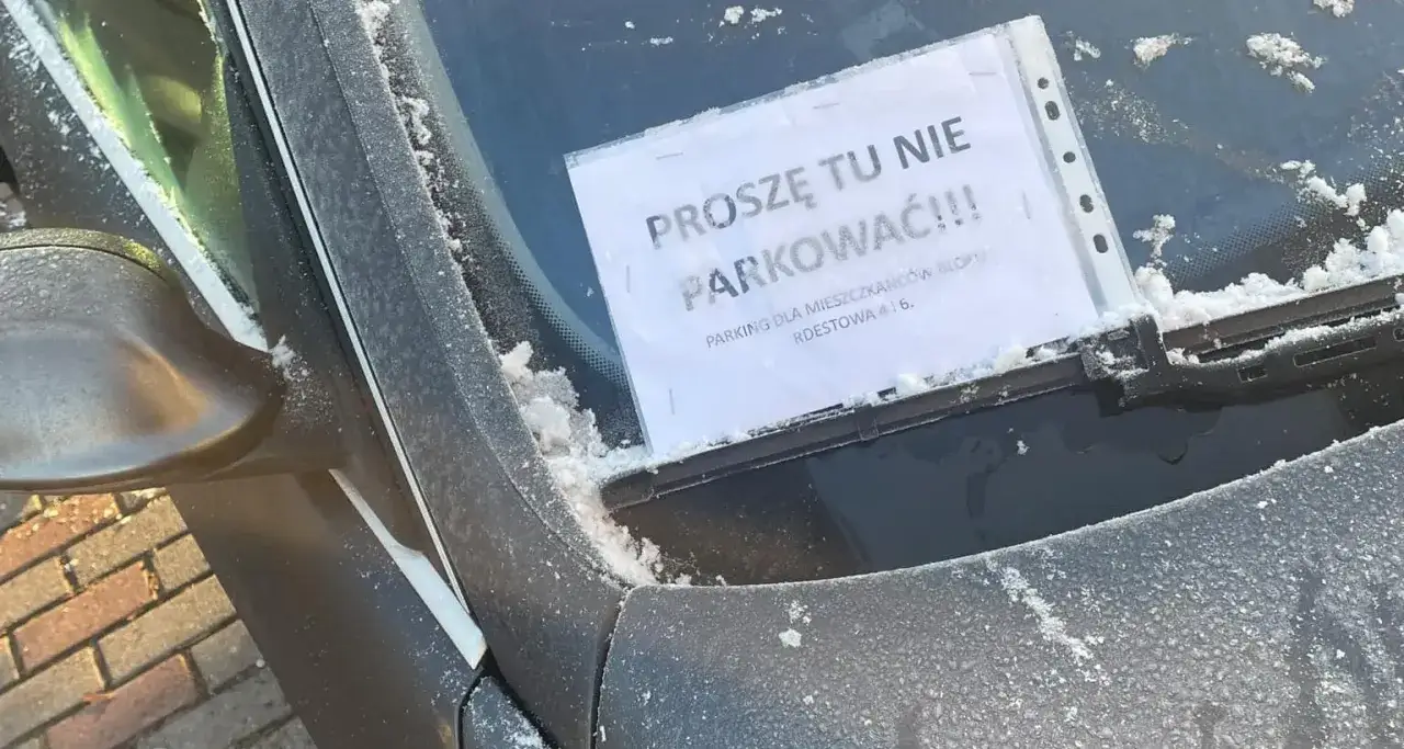 Na przedniej szybie samochodu, pokrytej szronem, wisi kartka z napisem