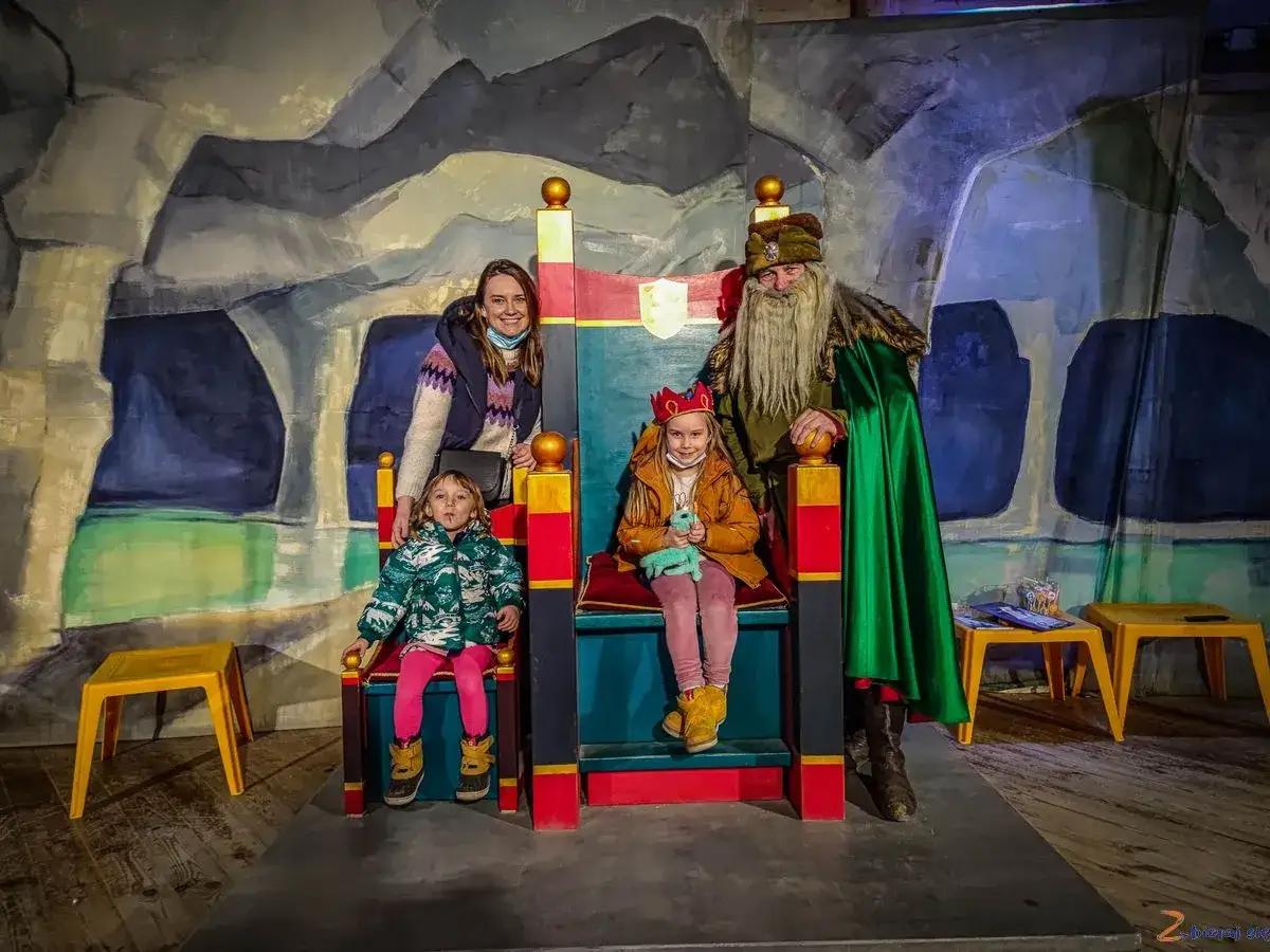 Rodzina w kopalni soli w Wieliczce spotyka kr&oacute;la. Dzieci siedzą na tronach, a mama i kr&oacute;l pozują do zdjęcia.