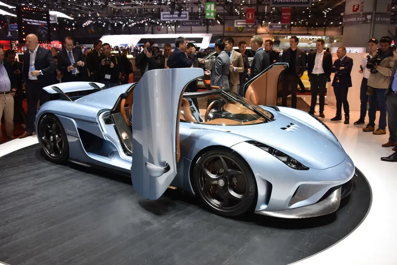 Błękitny Koenigsegg Regera z otwartymi drzwiami, prezentowany na wystawie samochodowej, przyciąga uwagę tłumu.