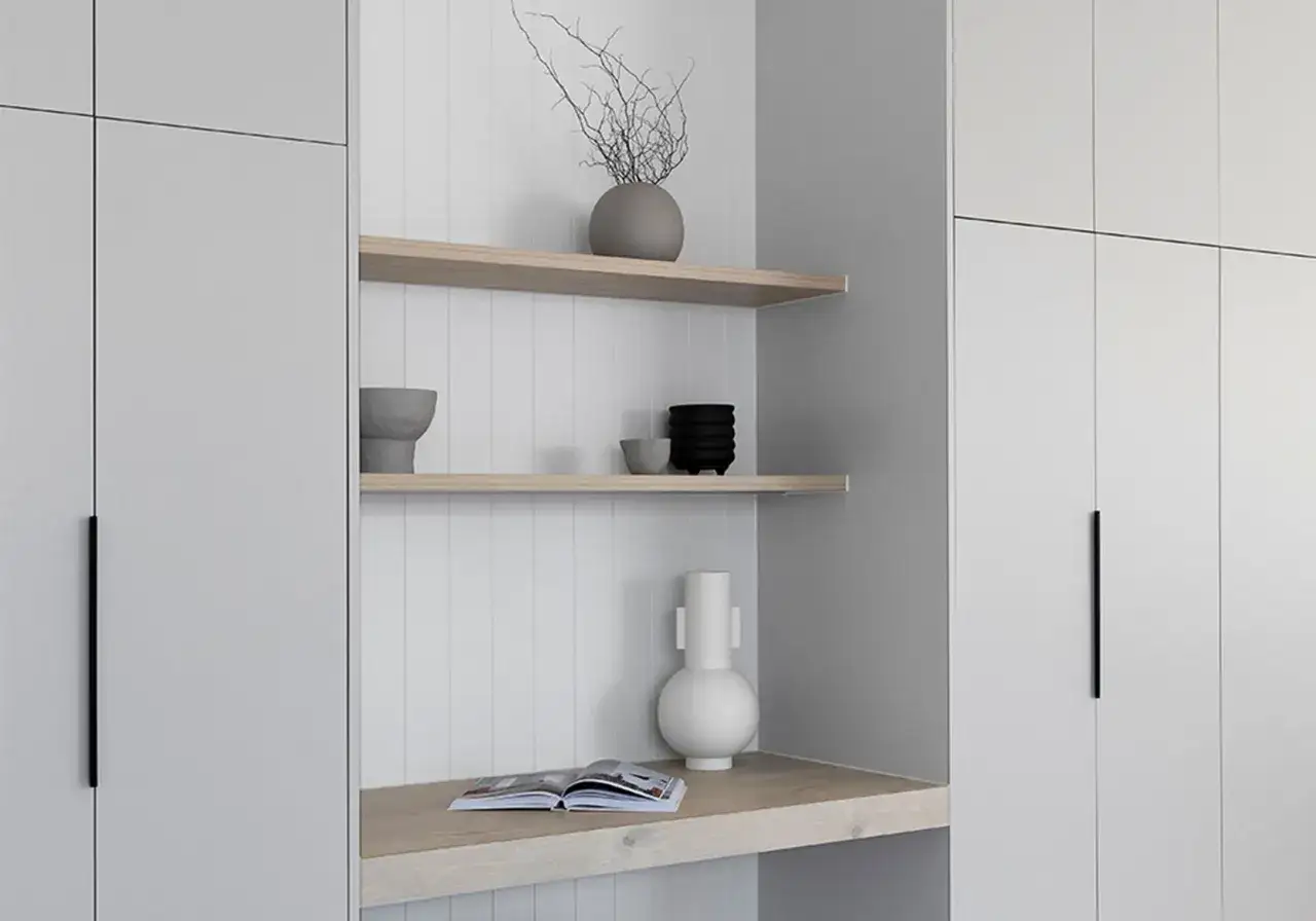 Minimalist shelves with decorative vases and a book sit above a wooden desk, integrated into a modern small house design with sleek grey cabinetry.