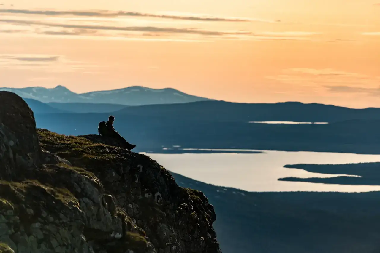 Vandrare vilar p&aring; en klippa med utsikt &ouml;ver V&aring;l&aring;dalens sj&ouml;ar och fj&auml;ll i solnedg&aring;ngen. En perfekt V&aring;l&aring;dalen vandring.