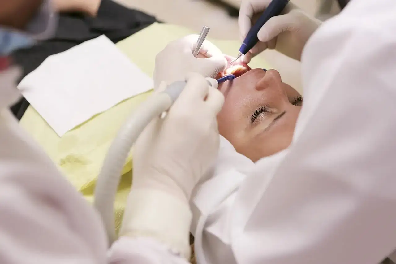 Dentysta używa narzędzi, by delikatnie wyciągnąć ropę z zęba pacjentki.