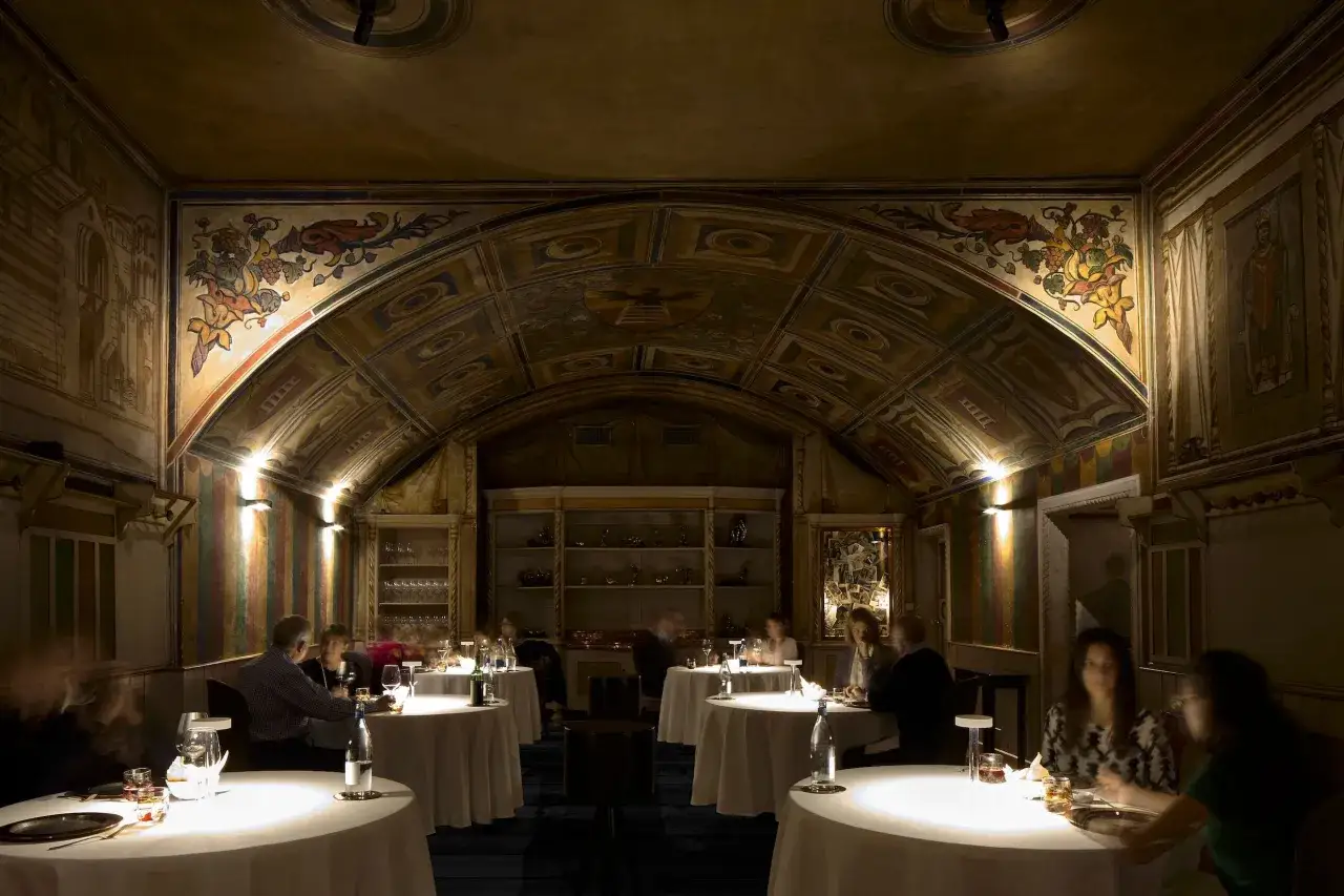 Atmosfera elegante in un ristorante con affreschi sul soffitto, dove i tavoli sono apparecchiati per una cena speciale. Un'esperienza culinaria degna delle **Perbellini stelle Michelin**.