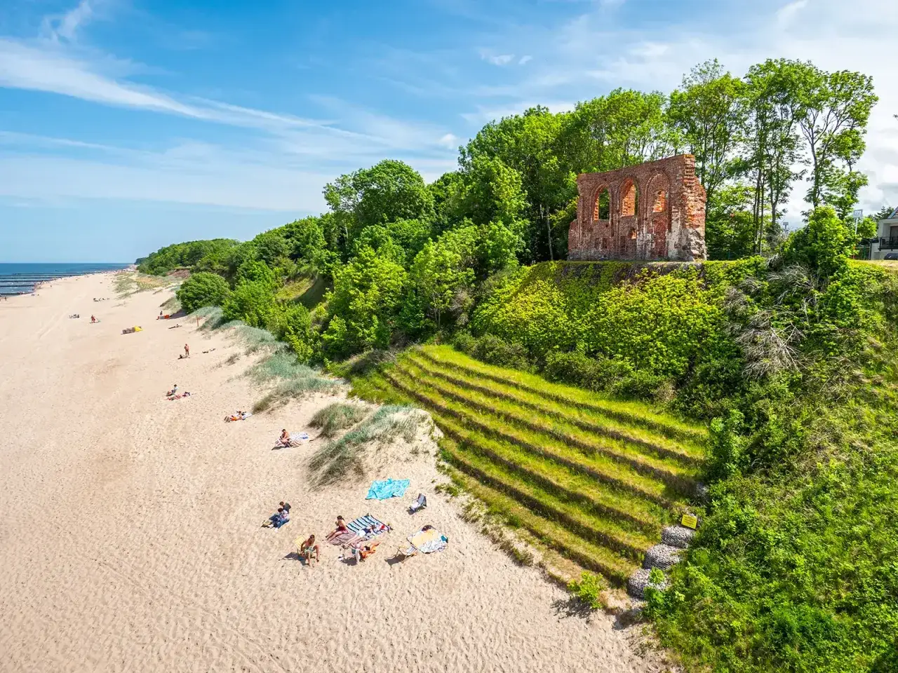 Piękny klif w Trzęsaczu z ruinami kościoła na szczycie. Na piaszczystej plaży odpoczywają turyści.