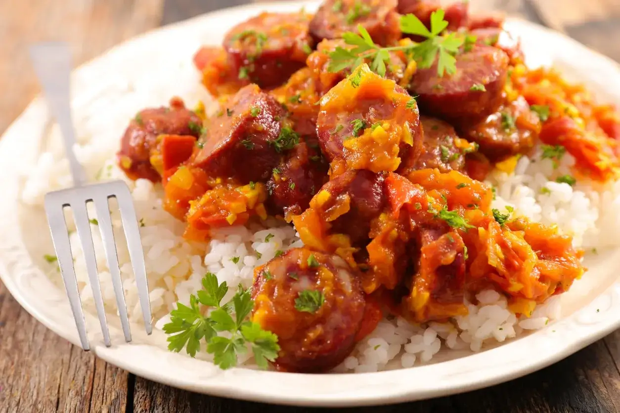 Assiette de riz blanc garnie de rougail saucisse, plat réunionnais savoureux, avec une touche de persil frais.