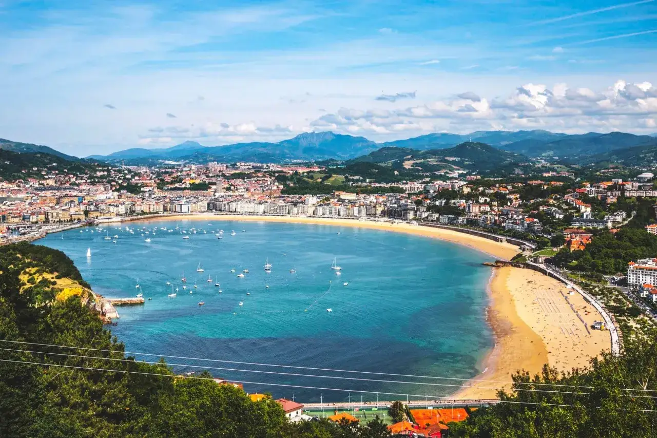 Bucht von San Sebasti&aacute;n mit La Concha Strand, vielen Segelbooten und gr&uuml;nen H&uuml;geln im Hintergrund.