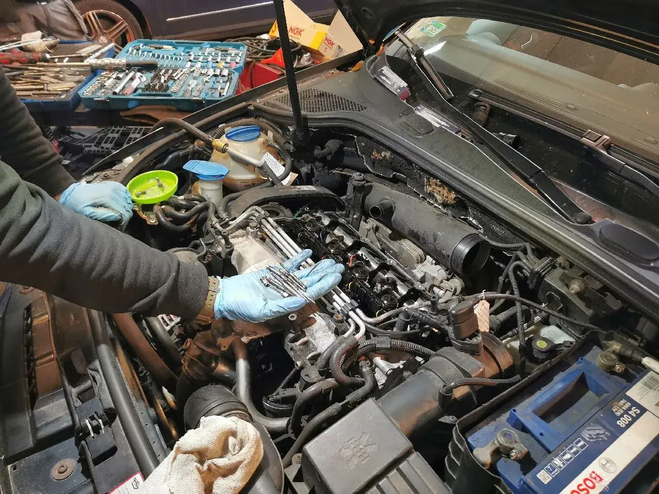 Mechanik w niebieskich rękawiczkach trzyma nowe świece żarowe, gotowe do wymiany w silniku samochodu.