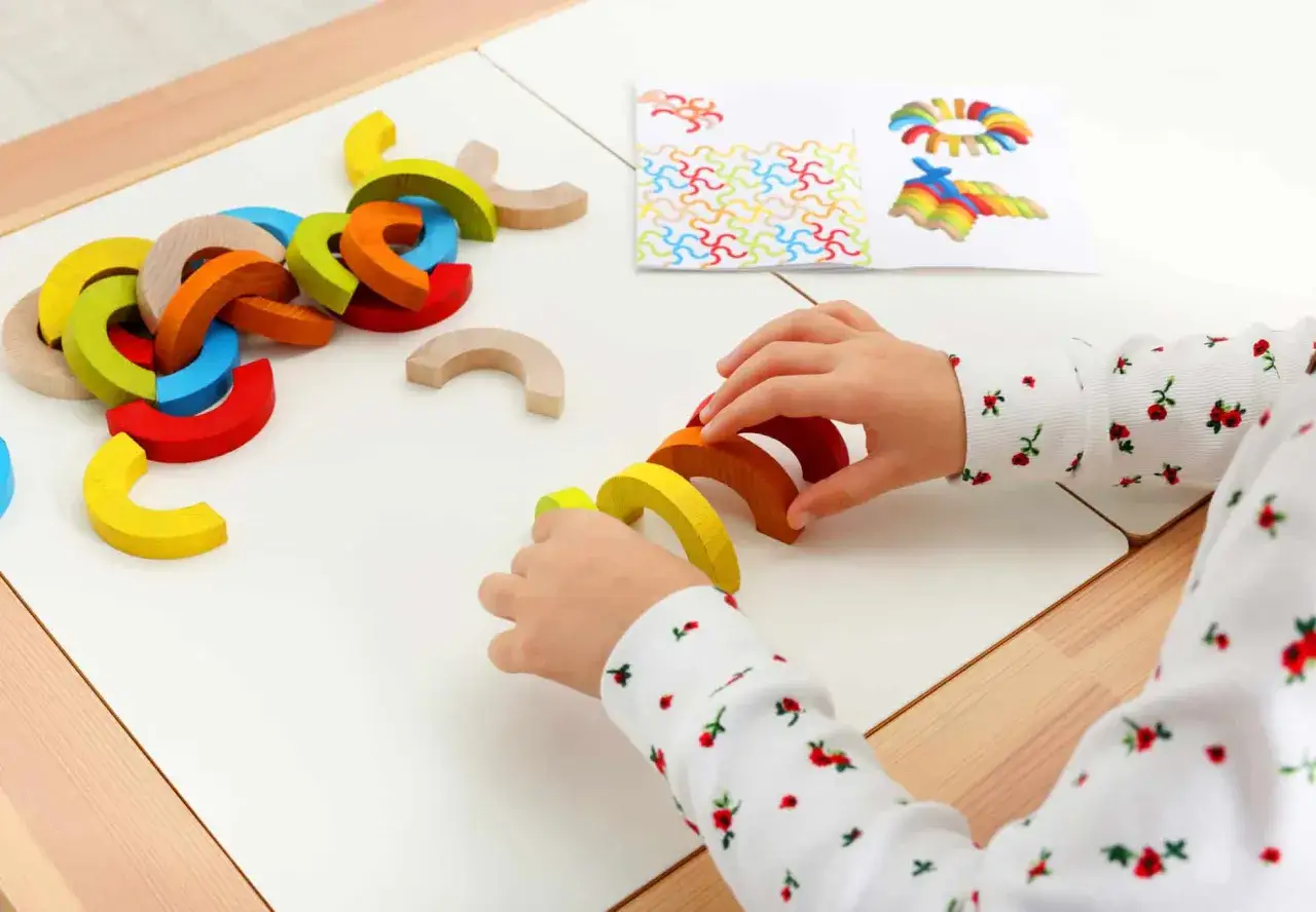 Manos de ni&ntilde;o jugando con bloques de arco&iacute;ris de madera, parte de una sesi&oacute;n de terapia ocupacional.
