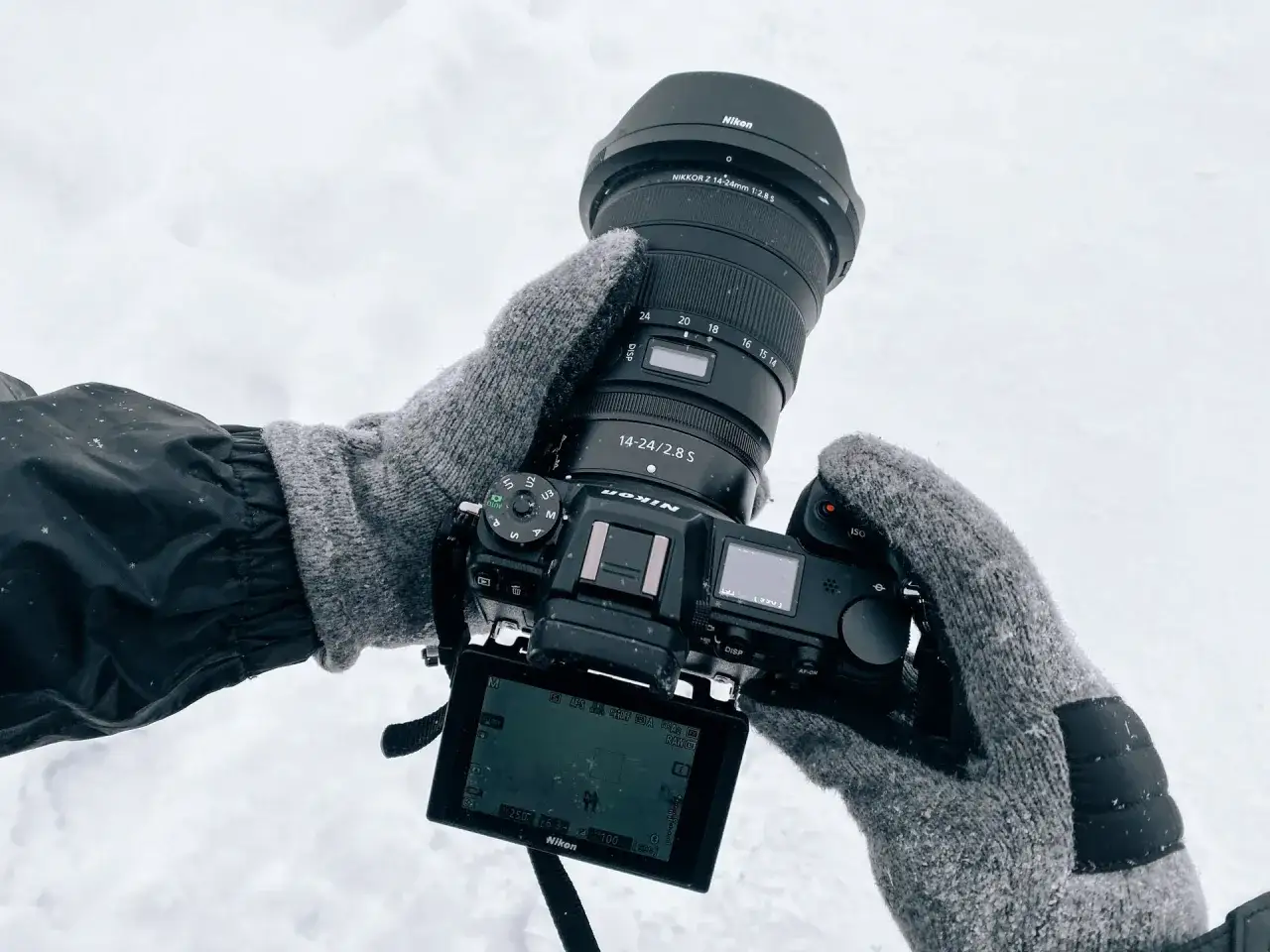 Ręce w zimowych rękawiczkach trzymają aparat Nikon Z6 II z obiektywem 14-24mm. Test sprzętu w śnieżnych warunkach.