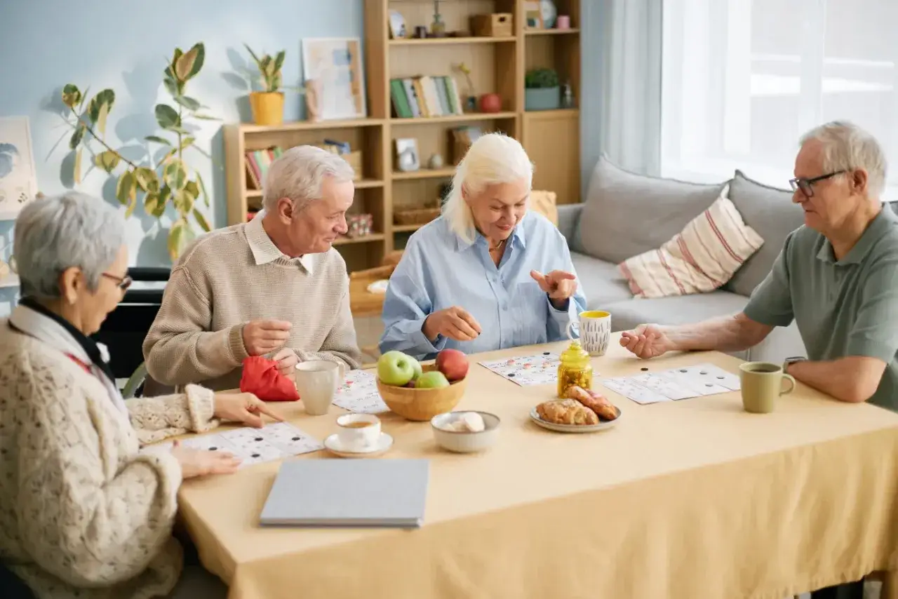 Seniorzy grają w bingo, ćwiczenia pamięci dla seniorów. Radość i skupienie przy stole pełnym smakołyków.
