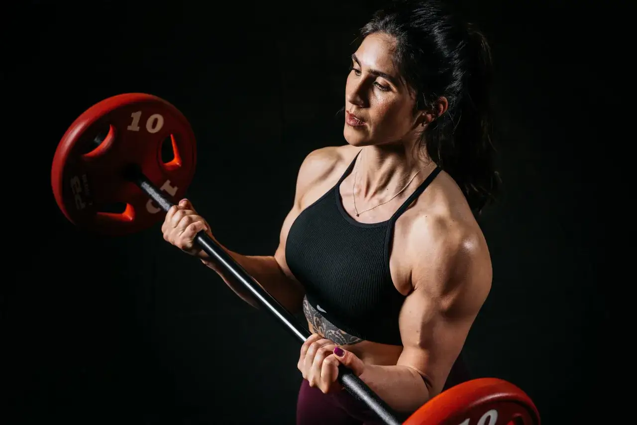 Eine Frau mit definierten Muskeln hebt eine Hantel. Ihr Bizeps ist stark ausgepr&auml;gt, w&auml;hrend sie sich auf ihr Training konzentriert.