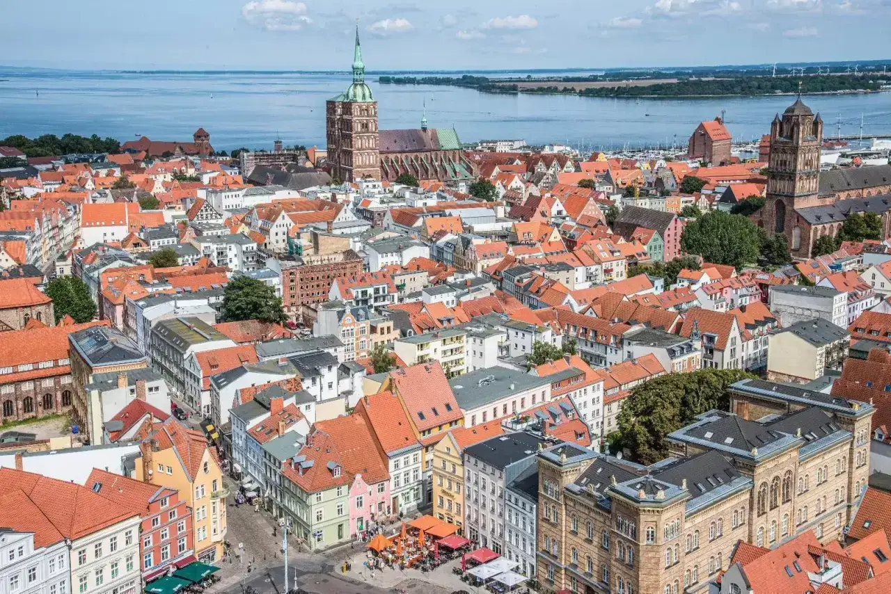 Blick &uuml;ber die roten D&auml;cher der **Stralsund Altstadt** mit Kircht&uuml;rmen und dem Wasser im Hintergrund.