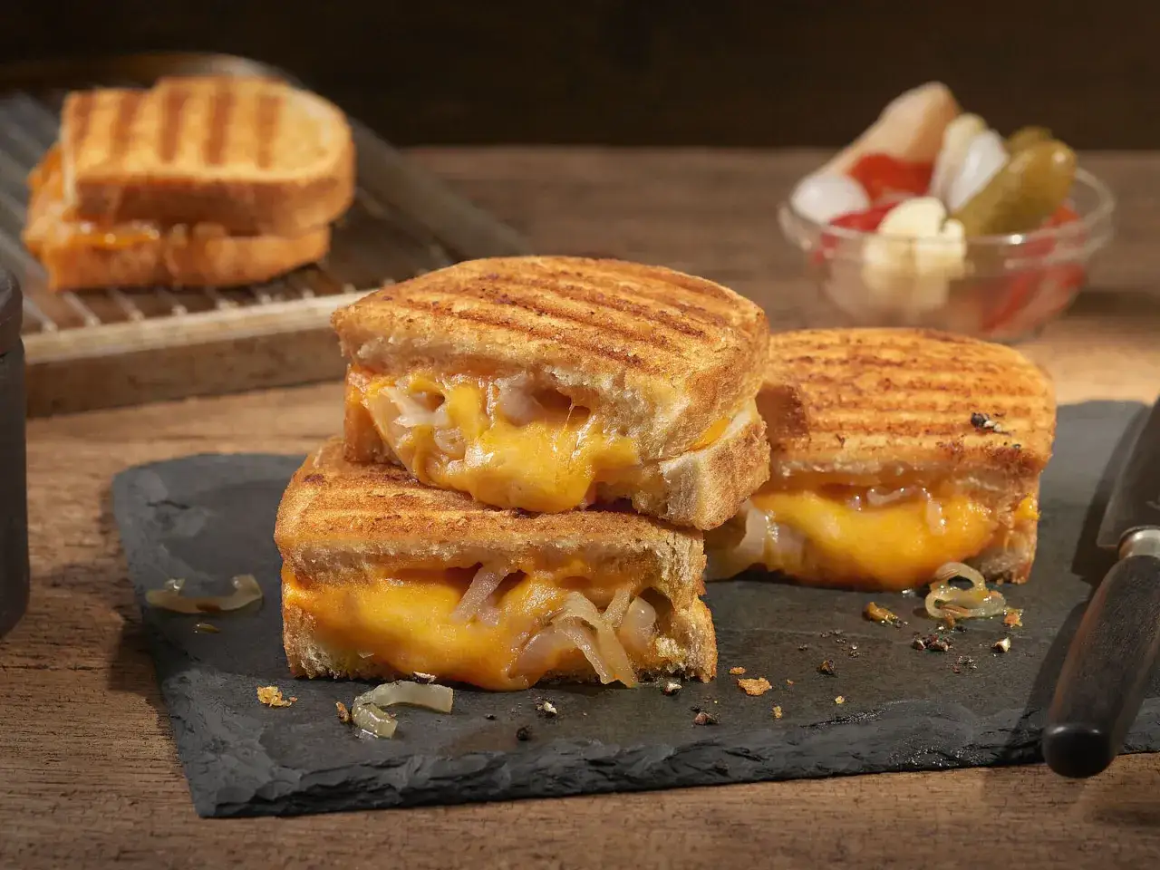 Perfektes grilled cheese sandwich rezept: goldbraun geröstetes Brot mit geschmolzenem Käse und karamellisierten Zwiebeln. Dazu eingelegtes Gemüse.