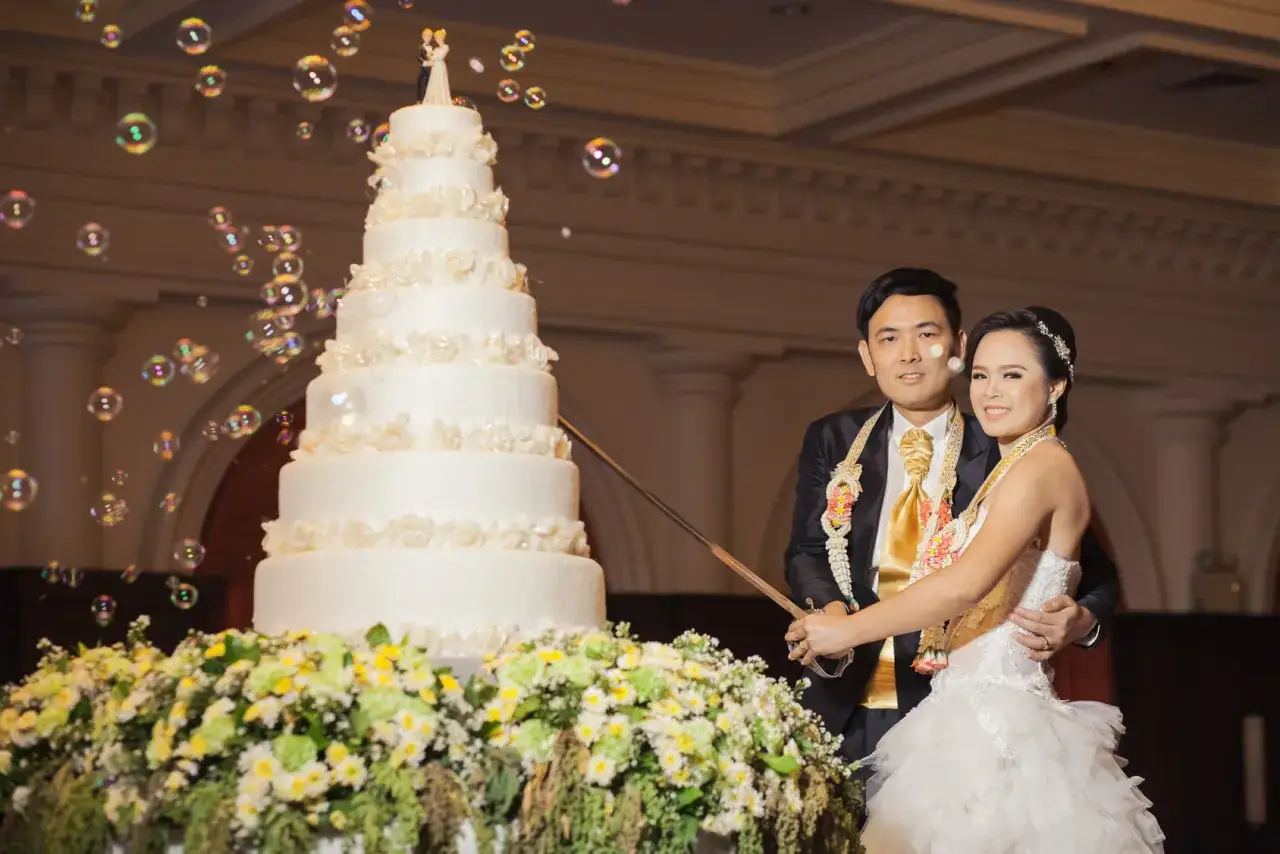 Ein Brautpaar feiert seine chinesische Hochzeit und schneidet gemeinsam die mehrstöckige Torte an, während Seifenblasen durch die Luft schweben.