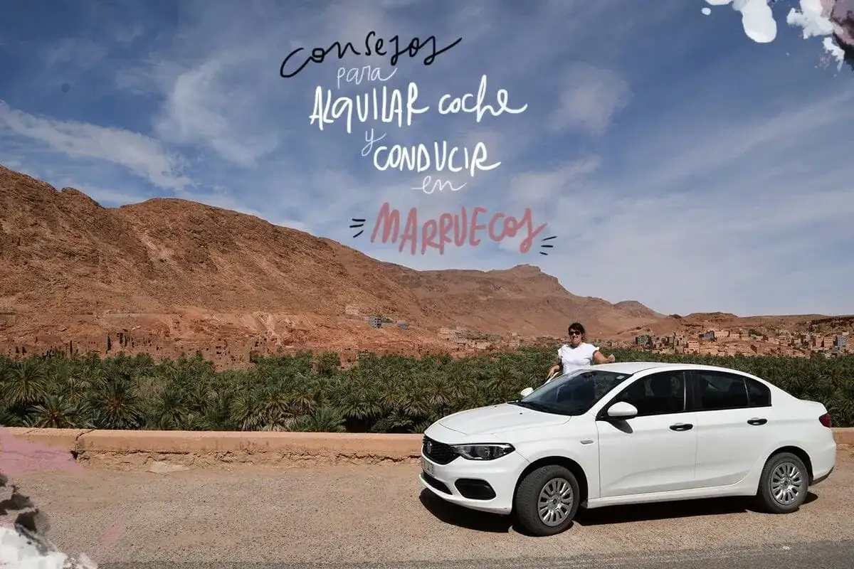 Mujer junto a coche blanco en Marruecos, lista para viajar. Paisaje desértico con palmeras y montañas.