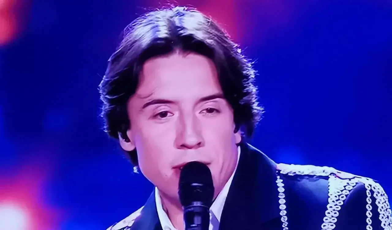 Młody mężczyzna śpiewa do mikrofonu. Czy to playback? W tle niebieskie światła.