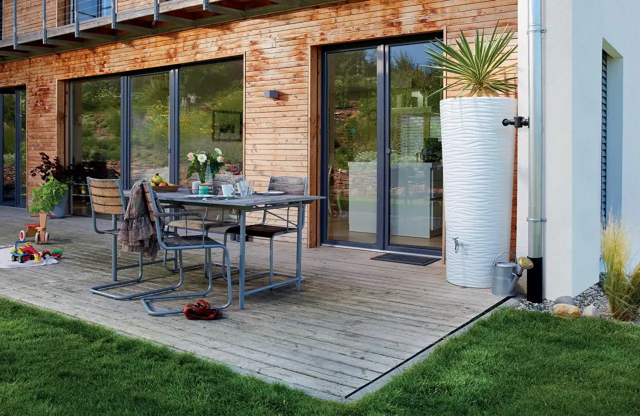 Installation r&eacute;cup&eacute;rateur eau de pluie : un grand r&eacute;servoir blanc textur&eacute; est raccord&eacute; &agrave; une goutti&egrave;re, pr&ecirc;t &agrave; collecter l'eau pour le jardin.