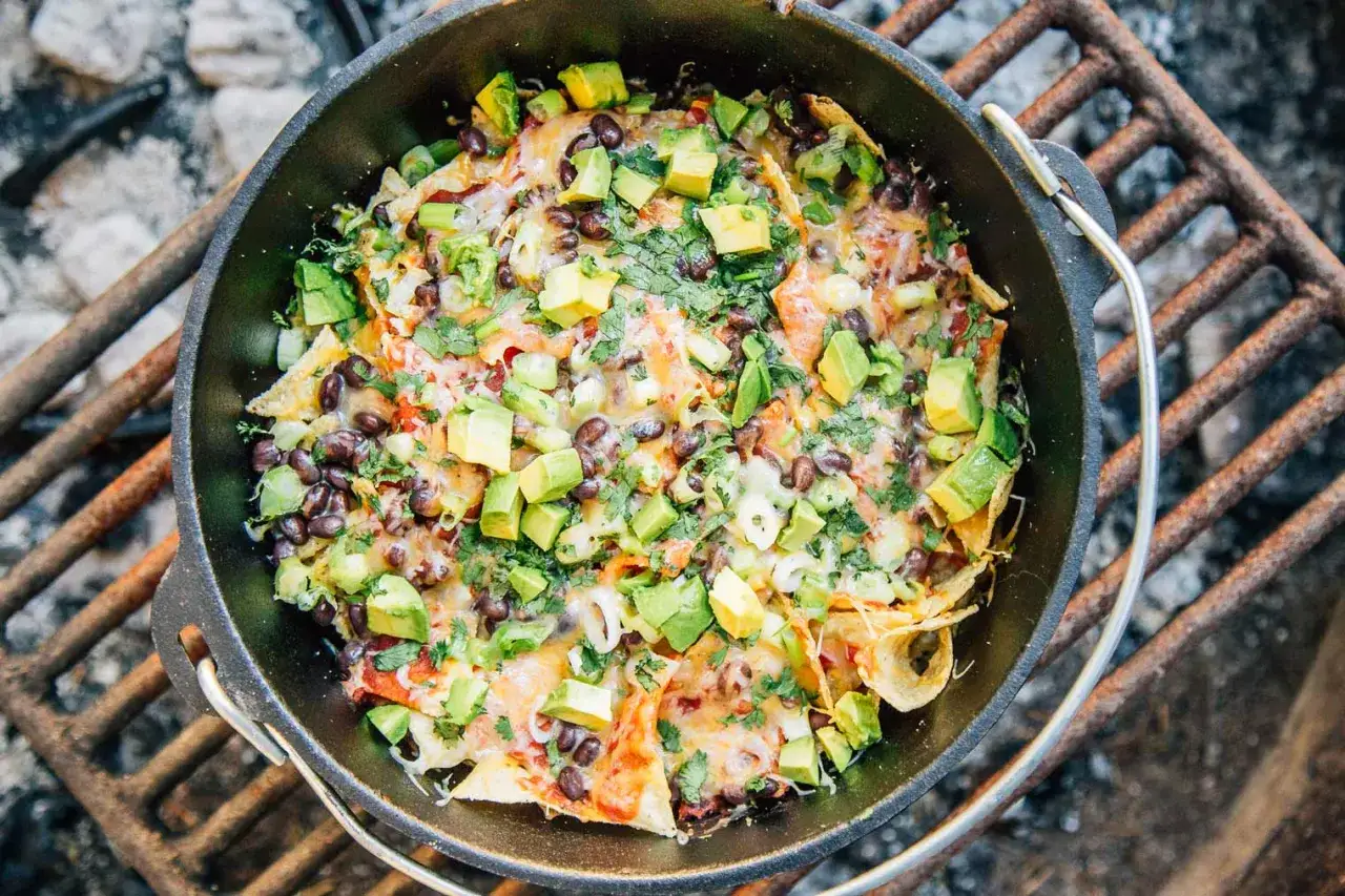 Schwarze Bohnen-Nachos mit Avocado und Koriander, zubereitet in einem Gusseisentopf &uuml;ber dem Feuer &ndash; ein perfektes Beispiel f&uuml;r einfache Outdoor-Gerichte.