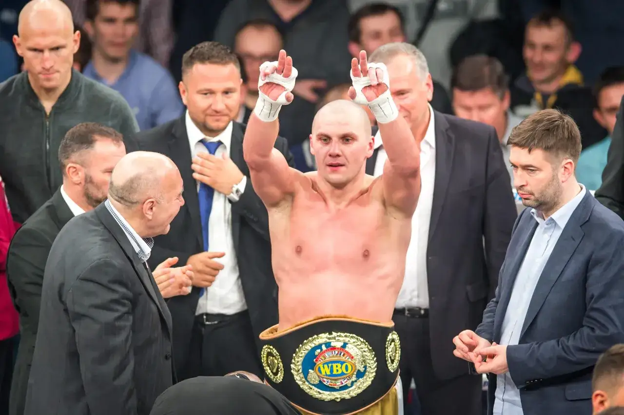 Bokser z pasem WBO świętuje zwycięstwo, otoczony przez ludzi w garniturach. Prawda o rzekomym zakazie wstępu dla Grzegorza Brauna na gale bokserskie pozostaje niejasna.