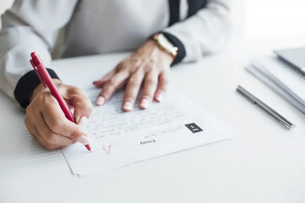Eine Hand mit rotem Stift korrigiert einen Aufsatz, vergibt eine 