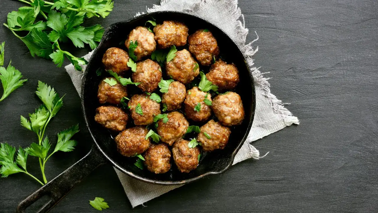 Deliziose polpette al forno, dorate e succulente, guarnite con prezzemolo fresco in una padella di ghisa.
