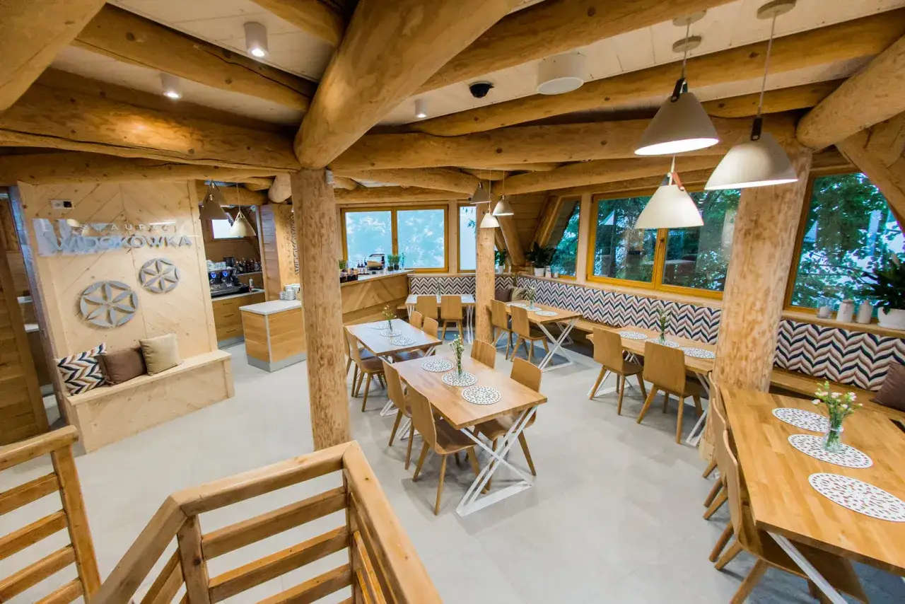 Drewniana restauracja Widok&oacute;wka z przytulnymi stolikami i widokiem na zieleń.