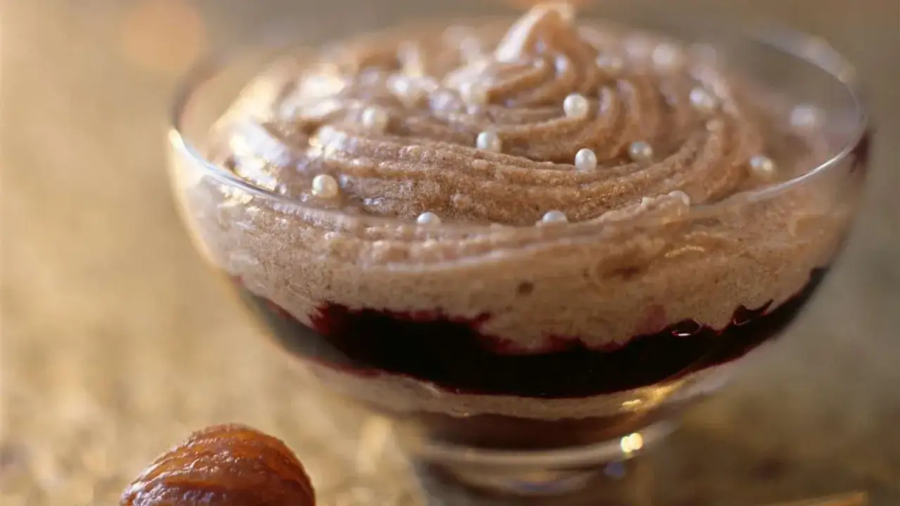 Delicioso mousse de casta&ntilde;as adornado con perlas comestibles, servido en copa de cristal con un toque de coulis de frutos rojos.