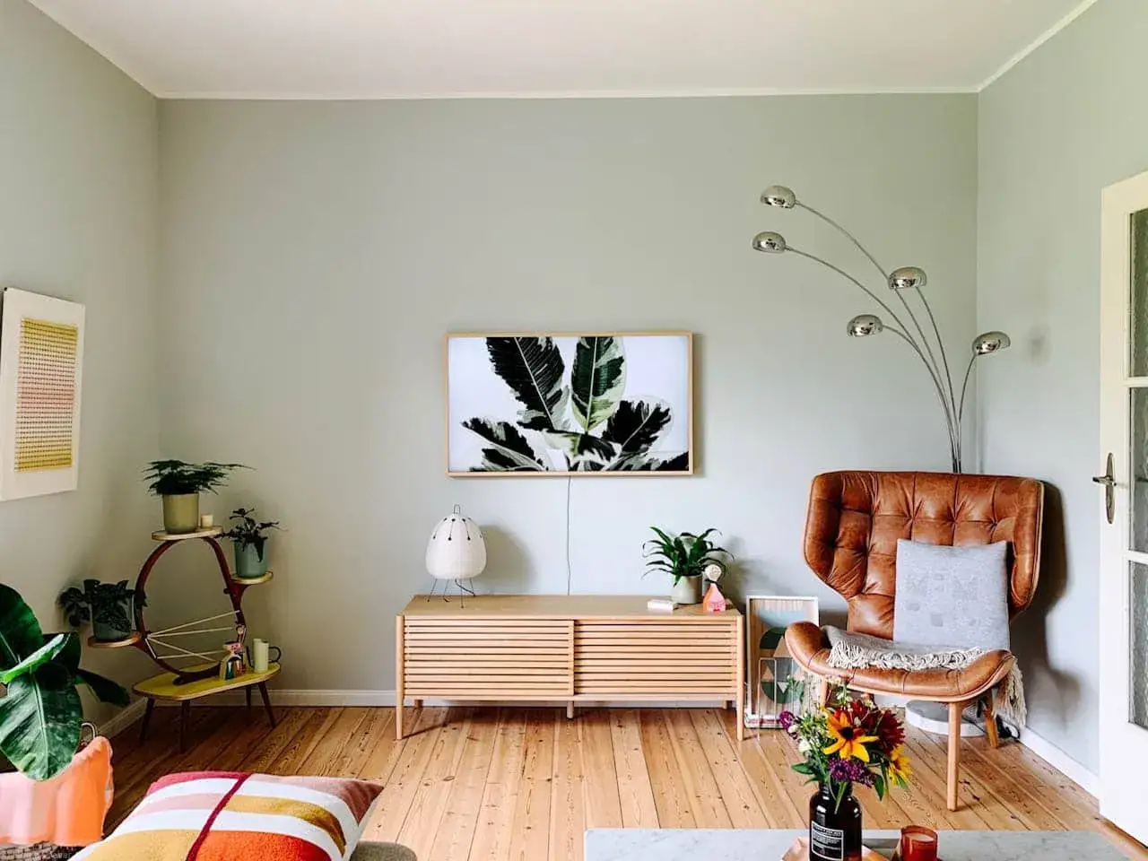 Gemütliches Wohnzimmer mit Ledersessel, Pflanzen und einem Bild von Blättern an der trend wand.