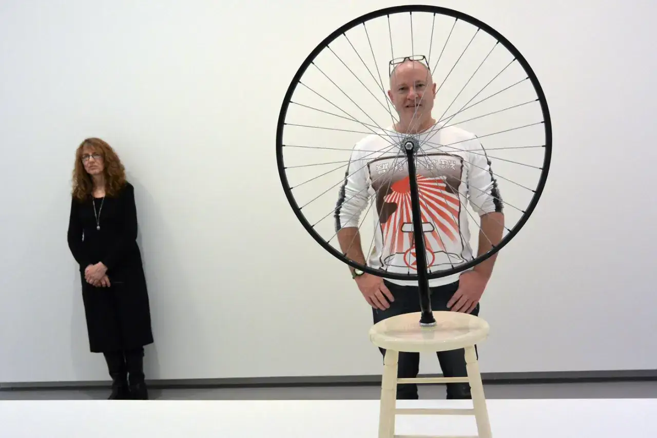 Un homme pose derri&egrave;re une roue de bicyclette duchamp, une femme en noir est &agrave; gauche.