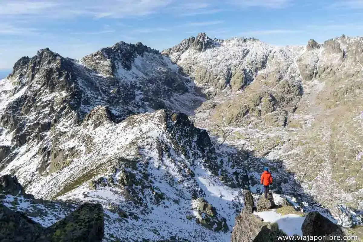 Senderismo en las rutas sierra de Gredos, con un montañero disfrutando del paisaje nevado y rocoso.
