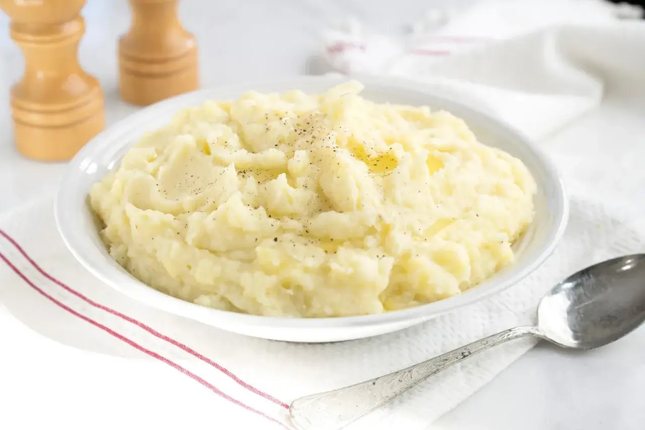 Un cremoso y reconfortante **puré de patatas** recién hecho, espolvoreado con pimienta negra, listo para ser servido.
