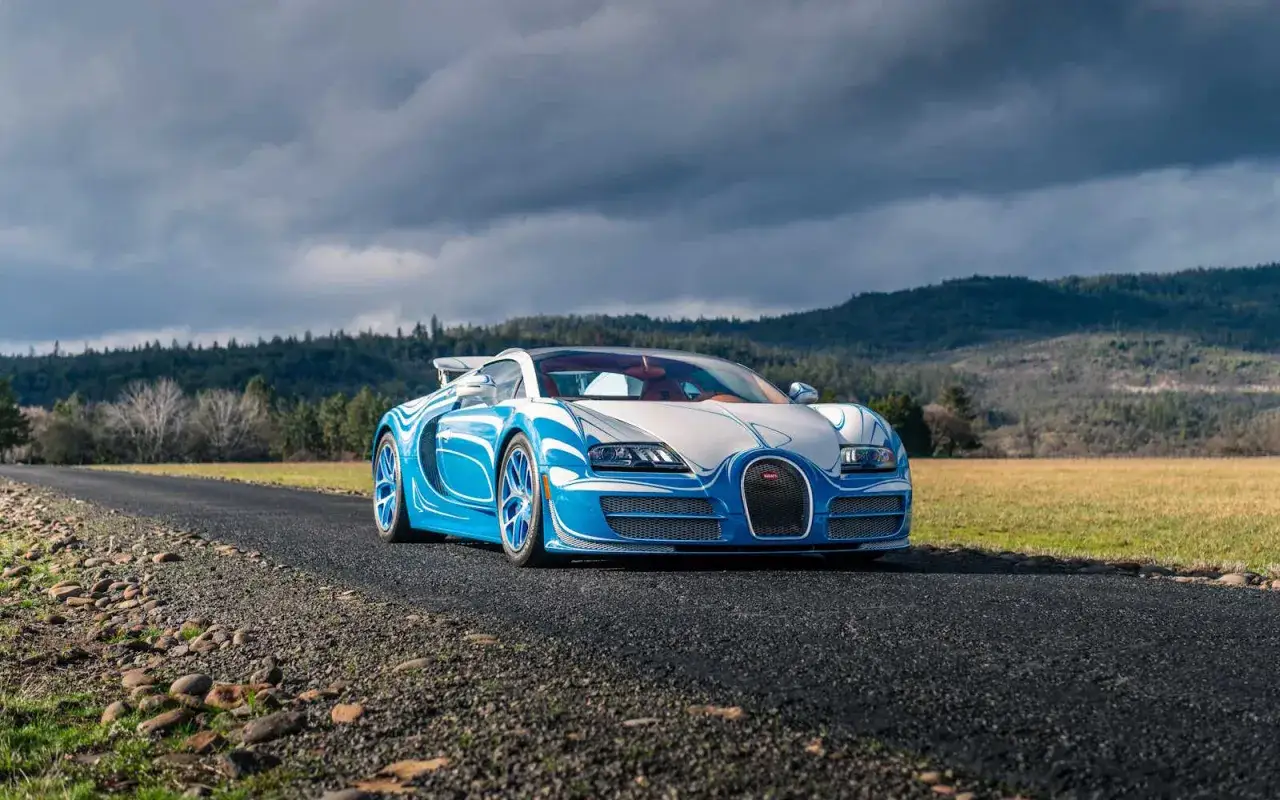 Niebiesko-biały Bugatti Veyron z unikalnym malowaniem na tle malowniczych wzgórz i burzowego nieba.