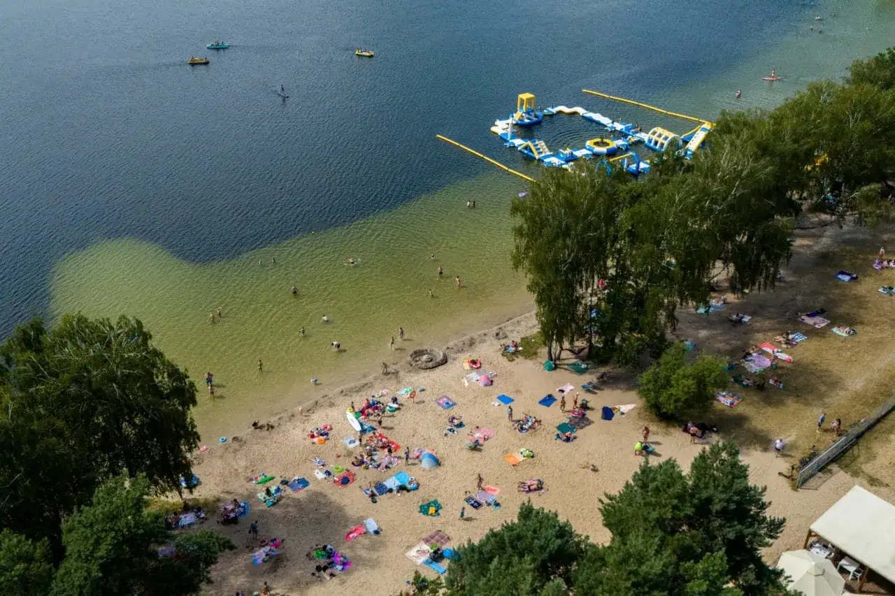 Letnie popołudnie nad jeziorem Zagnanie. Ludzie kąpią się, opalają na plaży i bawią na dmuchanym aquaparku.