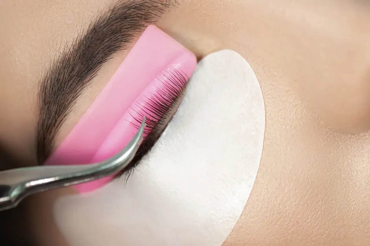 Application d'un rehaussement cil et teinture. Des cils sont courbés sur un support rose, prêts pour la teinture.