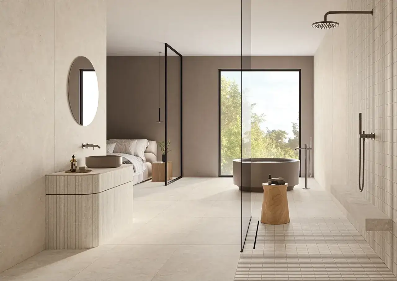 Salle de bain moderne avec baignoire, douche, lavabo et lit. Le sol et les murs sont recouverts de gr&egrave;s c&eacute;rame &eacute;maill&eacute; aux tons clairs.
