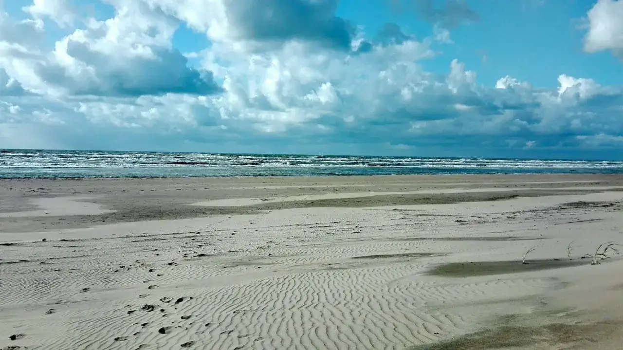Pusta plaża z falami i chmurami na niebie. Odpowiedź na pytanie: czy w Holandii jest morze? Tak, jest!