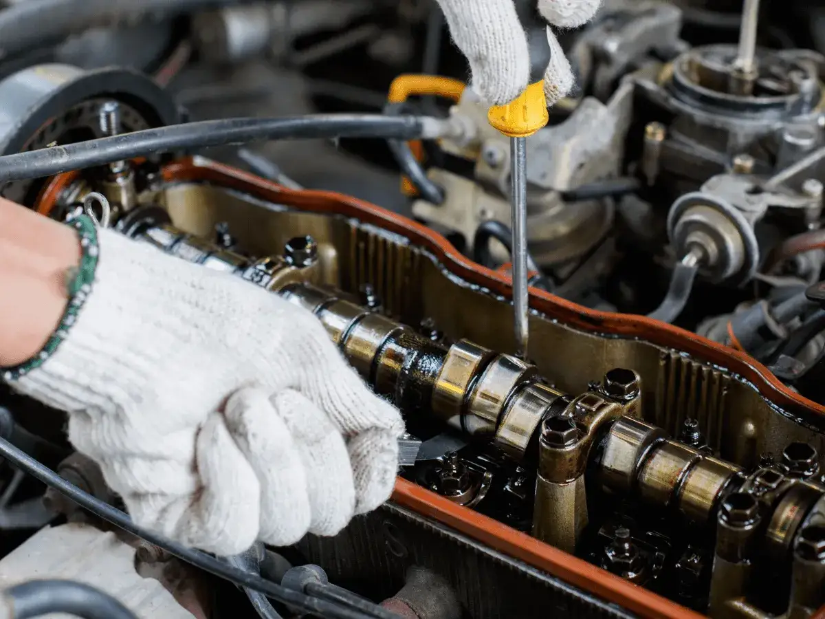 Mechanik w białej rękawiczce reguluje luzy zaworowe w silniku, używając śrubokręta.