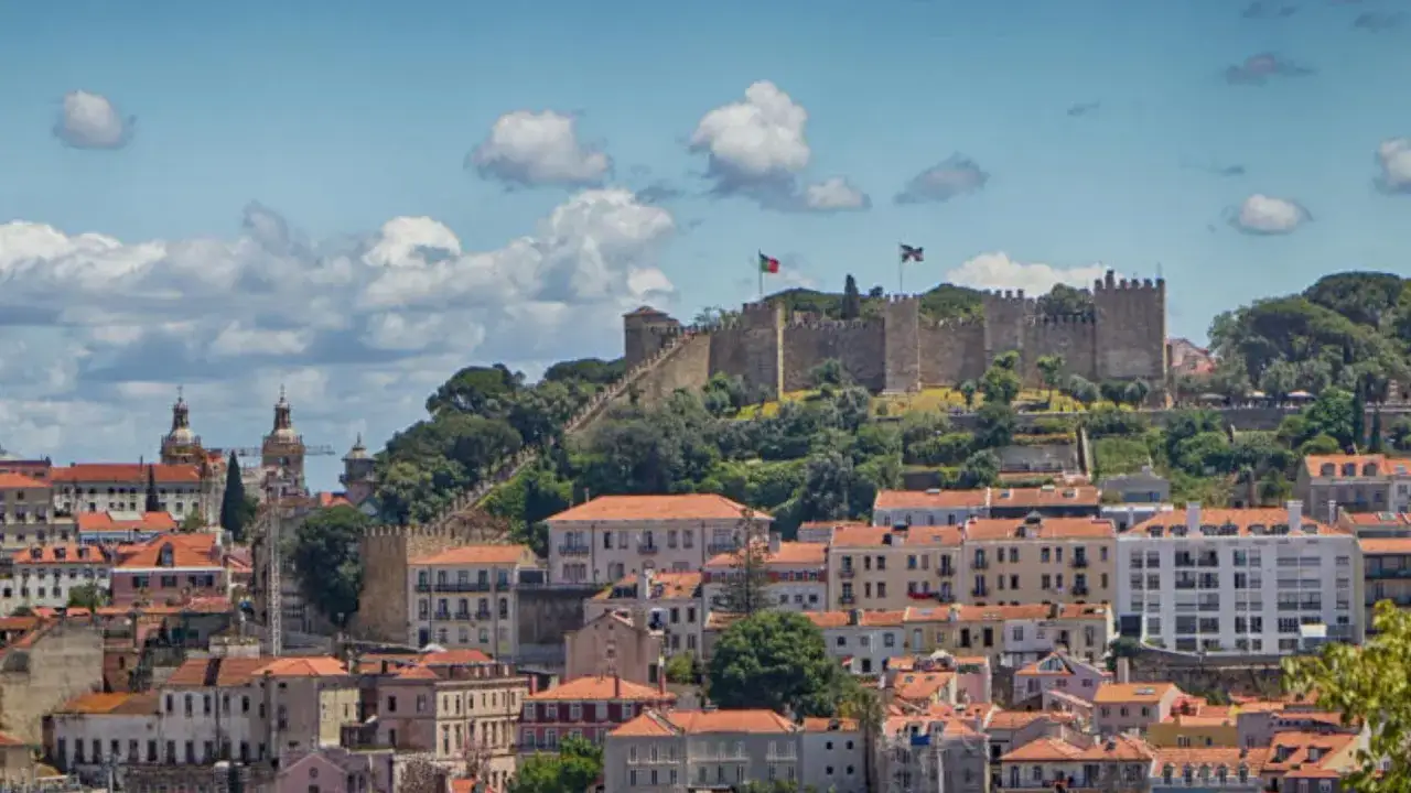 Blick auf Lissabon mit dem Castelo de S&atilde;o Jorge auf dem H&uuml;gel, umgeben von roten D&auml;chern und gr&uuml;nen B&auml;umen.