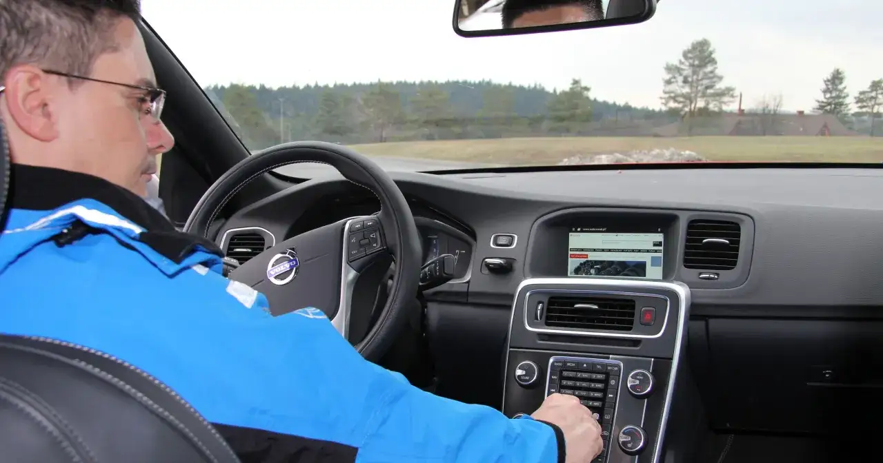 Wnętrze Volvo z ekranem pokazującym Android Auto. Kierowca w niebieskiej kurtce obsługuje panel.