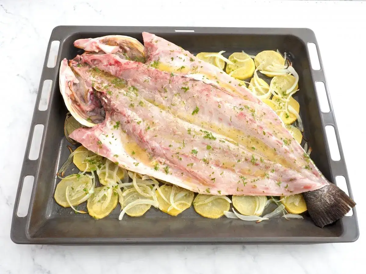 Corvina entera preparada en bandeja para hornear con patatas y cebolla. Una de las recetas de corvina más sencillas.
