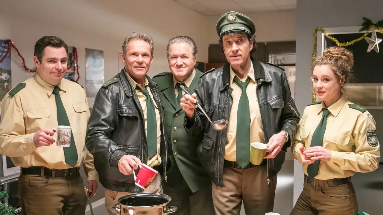 Hubert und Staller mit Kollegen in Uniformen, die sich an einem Topf mit Getr&auml;nk bedienen.
