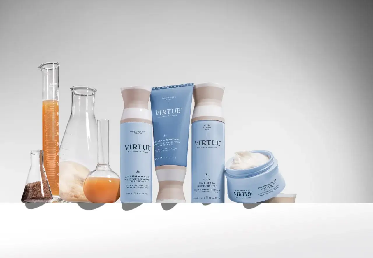 Produkty Virtue do walki z przesuszona skóra głowy: szampon, odżywka, suchy szampon i peeling. W tle naczynia laboratoryjne z płynami.