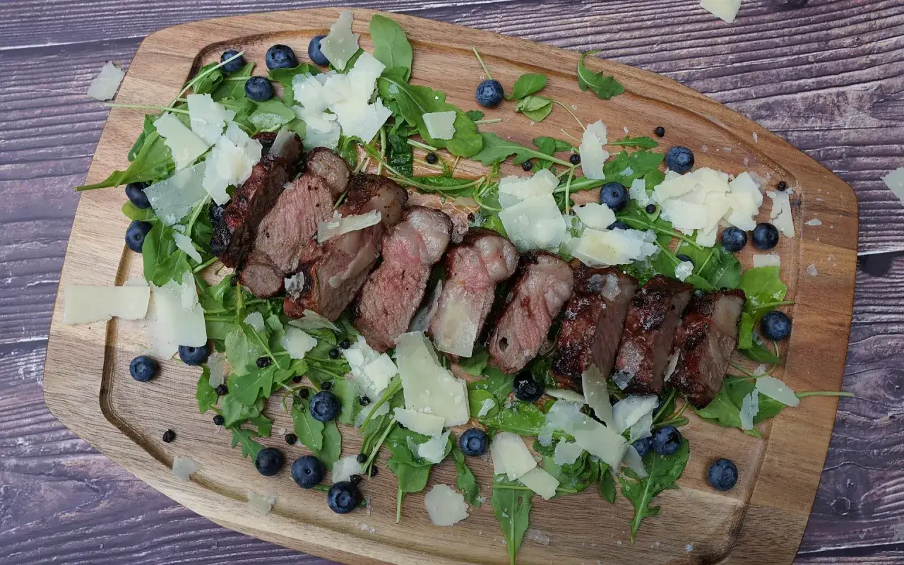 Perfekte Tagliata di manzo auf Rucolabett mit Blaubeeren und Parmesan-Spänen.